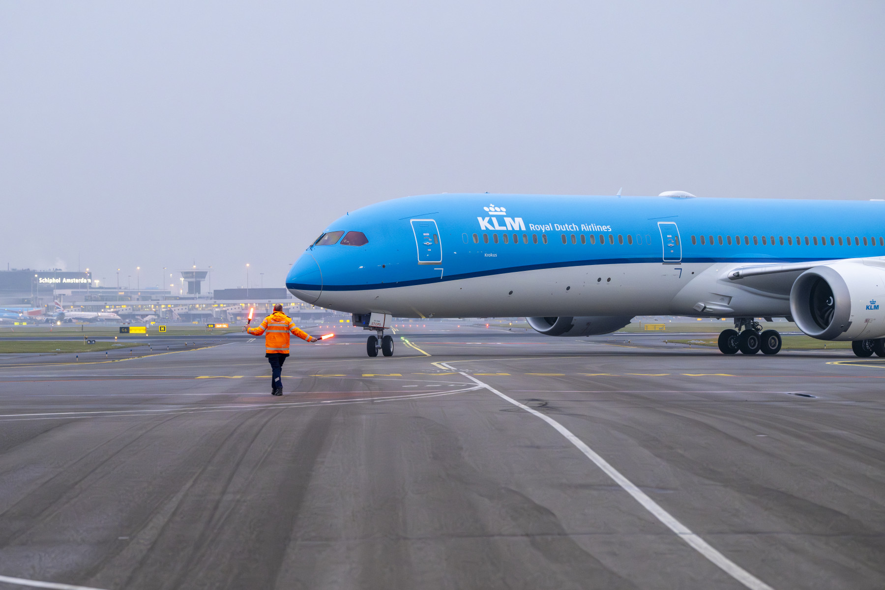 KLM Boeing 787 Dreamliner named Krokus guided by ground crew in orange vest at Amsterdam Schiphol Airport, terminal in background
